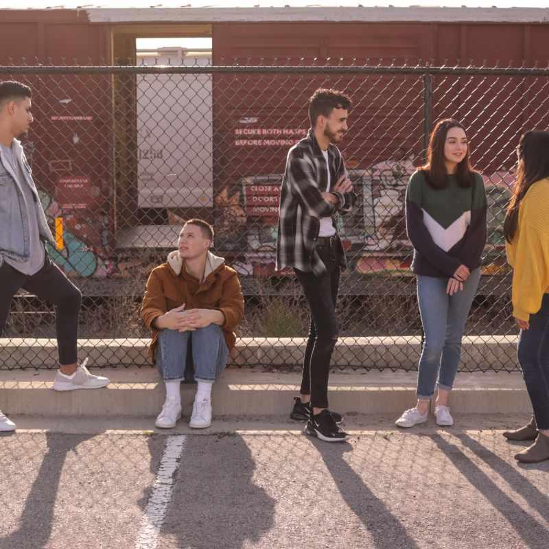 Group of young adults talking and hanging out near a fence on a sunny day.